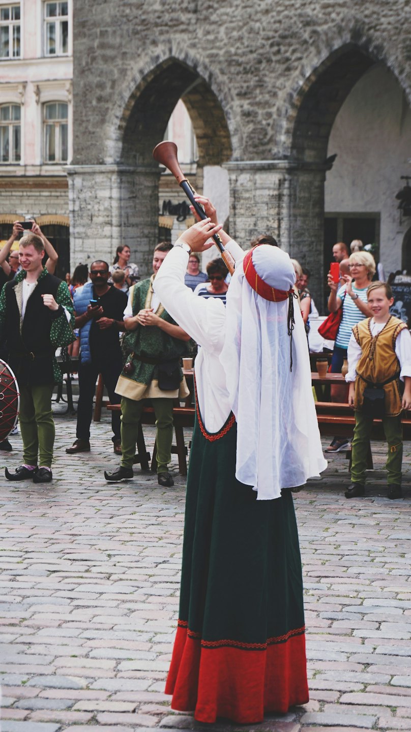 Musiker in mittelalterlicher Kleidung spielt auf einem gepflasterten Platz ein Horn.