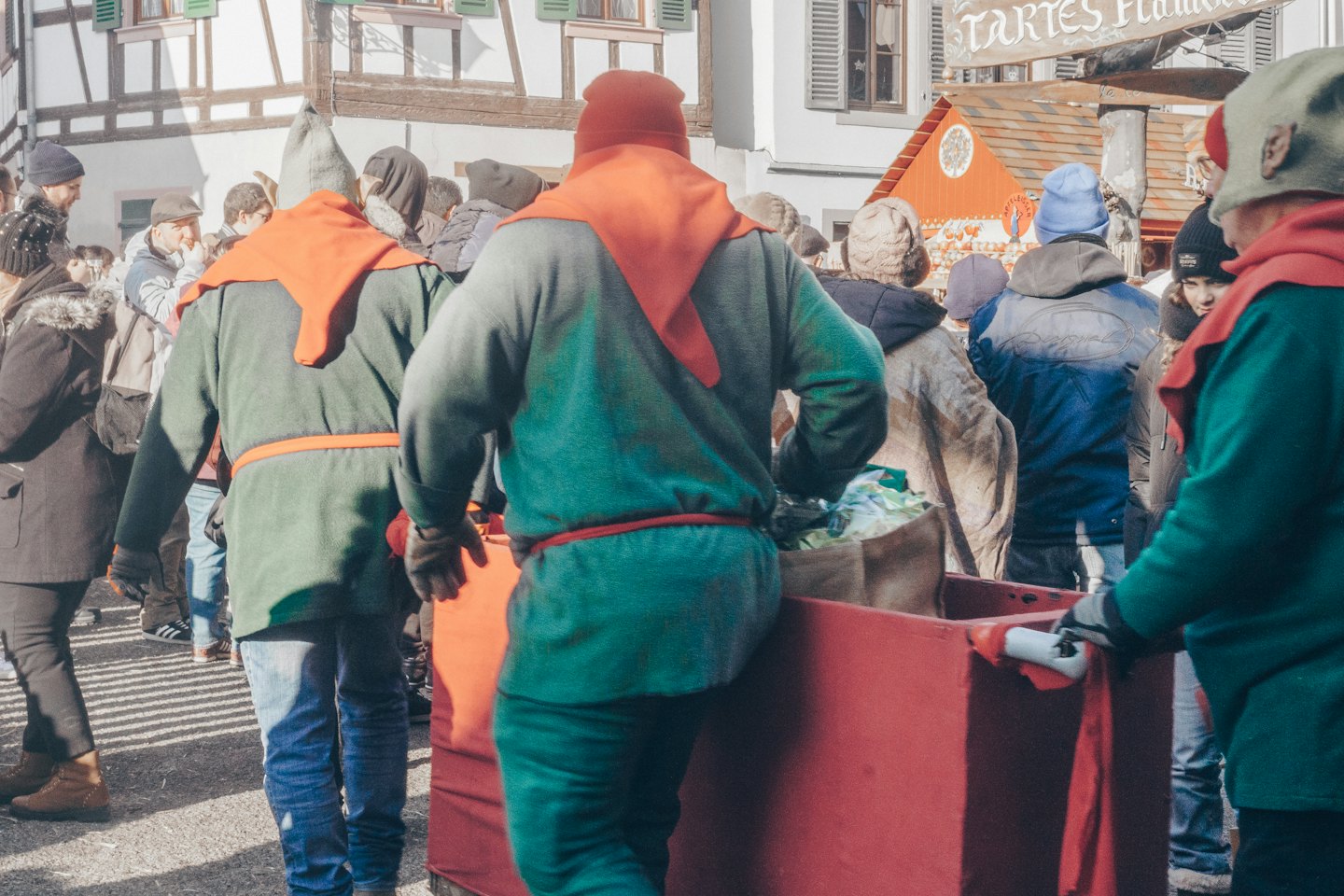 Menschen in mittelalterlichen Kostümen schieben rote Karren durch einen belebten Markt.